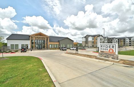 Front entrance of Ryder Ridge showcasing the modern clubhouse, community sign, and spacious driveway under bright Texas skies.