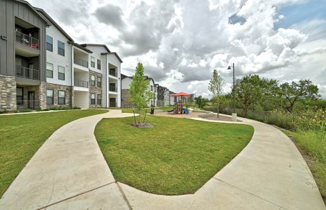 Peaceful outdoor courtyard at Ryder Ridge featuring green lawns, walking paths, and modern apartment buildings under a partly cloudy sky.