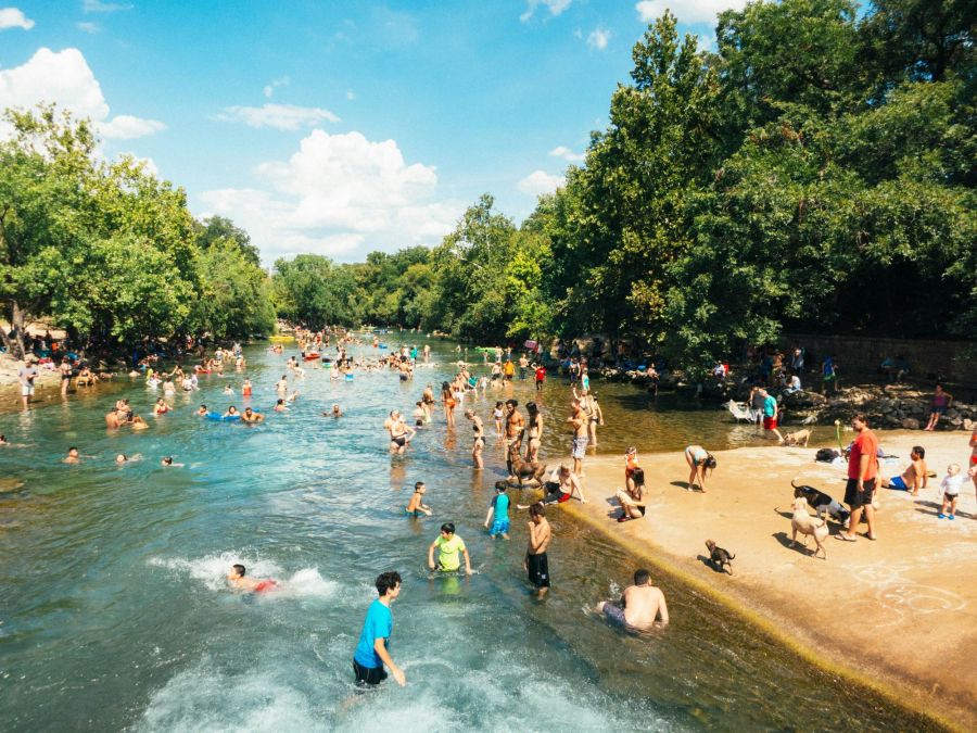 People swimming and relaxing at Barton Springs Pool in Austin, Texas, surrounded by trees and sunny skies near Ryder Ridge.