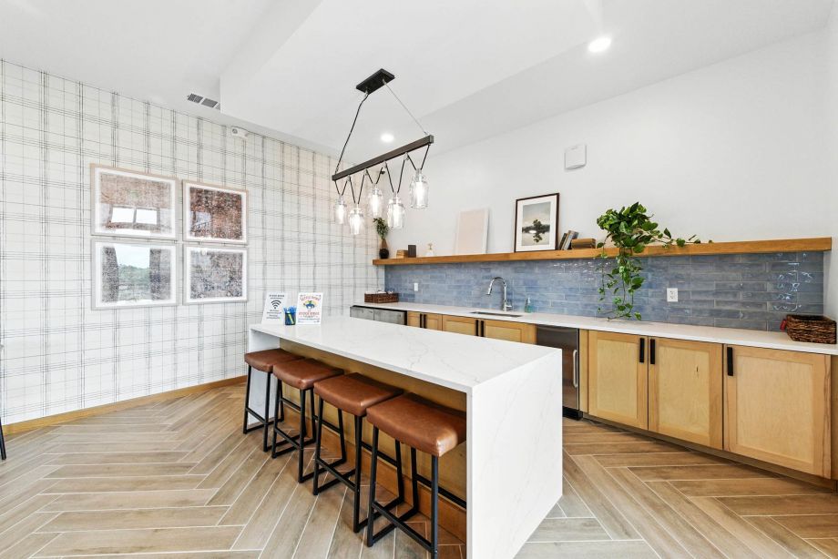 Community kitchen at Ryder Ridge featuring a large island with leather barstools, modern lighting, and wood-style cabinetry.