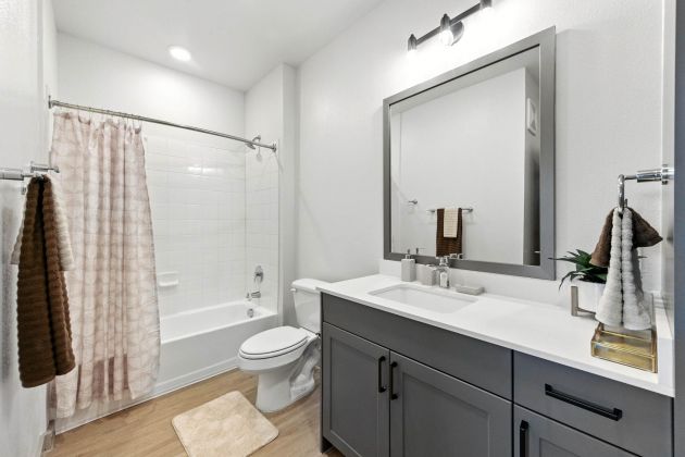 Modern bathroom at Ryder Ridge featuring a large vanity with gray cabinetry, bright lighting, and a tiled shower-tub combo.
